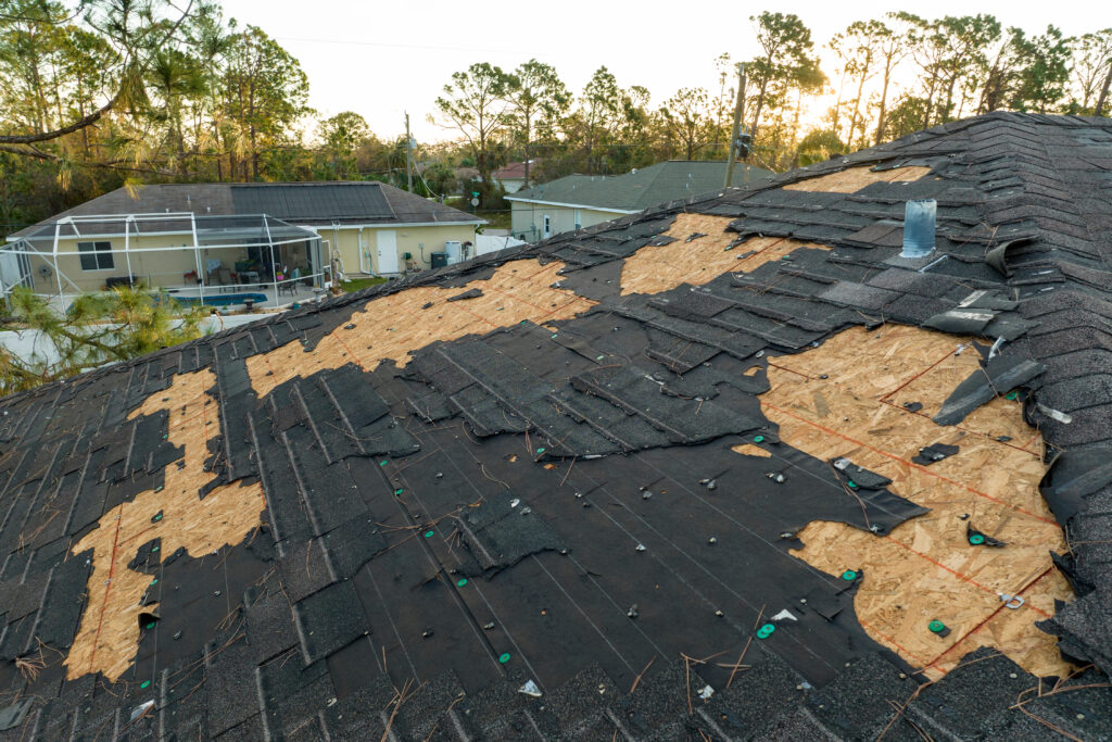 Ruined Rooftop in Need of Repair. Wind Damaged House Roof with Missing Asphalt Shingles and Exposed Decking After Hurricane Ian in Florida.